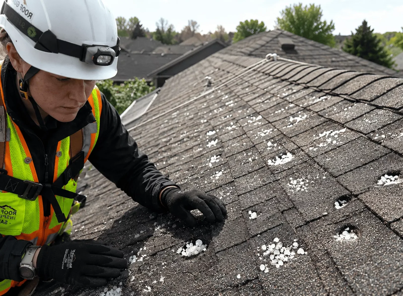 Roofer inspecting hail damage on residential shingle roof